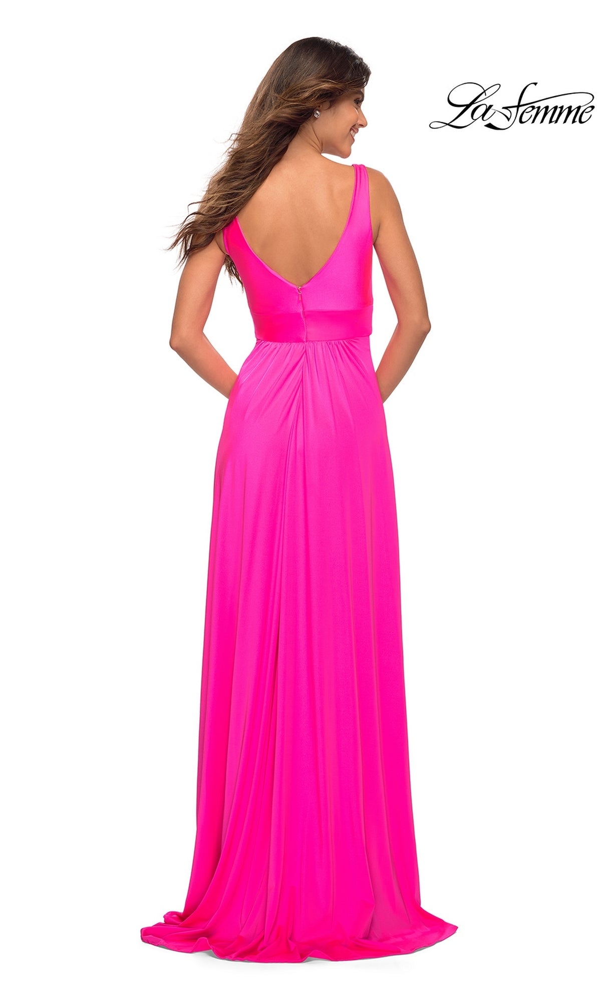 A woman stands facing away in the La Femme Neon Pink Long A-Line Prom Dress 30669, a floor-length sleeveless gown with a deep V-back. The